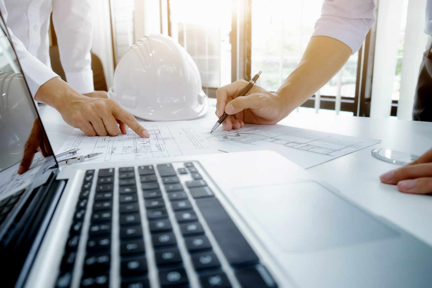Dos personas revisando los planos de una obra sobre una mesa, con un casco de seguridad blanco y un portátil